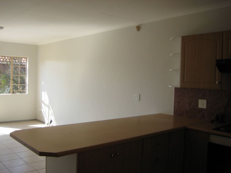 An open-plan kitchen area featuring wooden cabinetry, a laminate breakfast bar, and tiled flooring, offering a functional space ready for personalization.