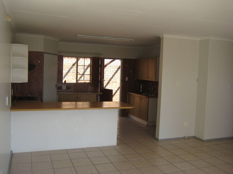 Open plan kitchen and living area featuring tiled flooring, built-in wooden cabinetry, a breakfast bar, and direct access to the exterior.
