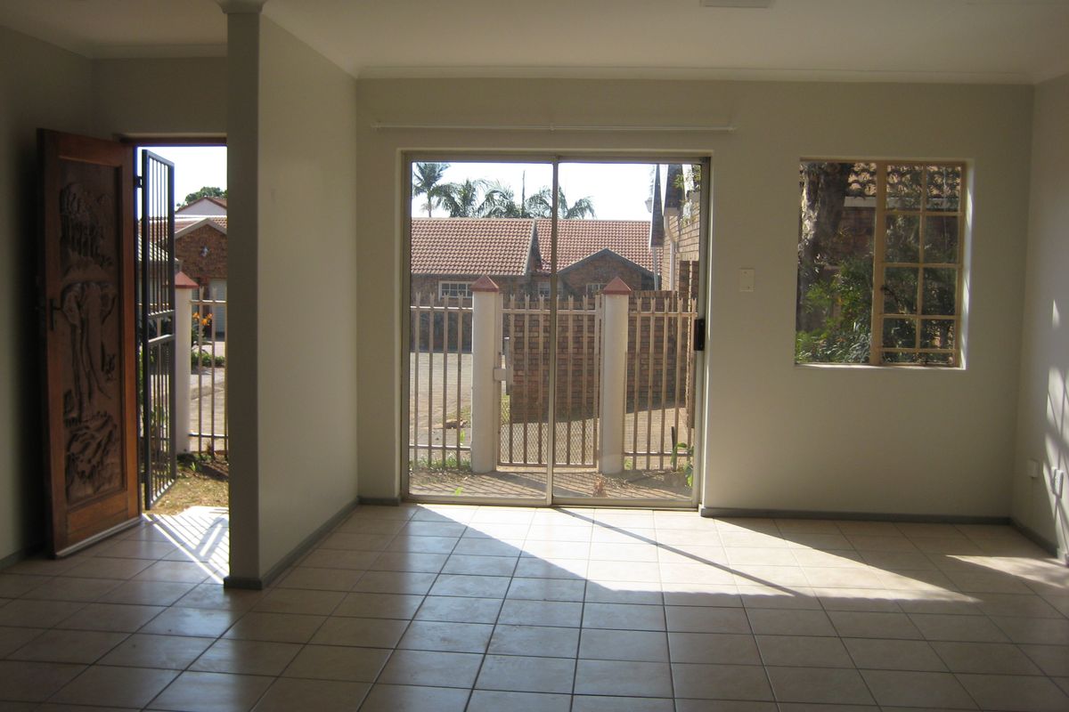 An empty, sunlit living area featuring neutral tiled flooring, a decorative carved wooden entrance door, and sliding glass doors leading to the exterior.