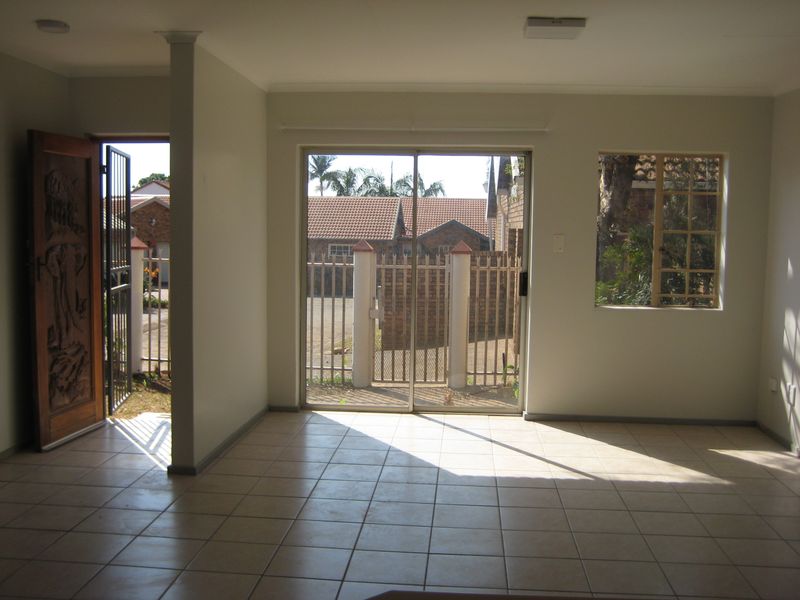 An empty, sunlit living area featuring neutral tiled flooring, a decorative carved wooden entrance door, and sliding glass doors leading to the exterior.