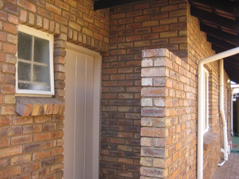 A view of the rear exterior facade featuring face brick construction, exposed timber rafters, and a functional rainwater downpipe system.