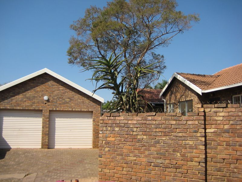Front exterior view of the property featuring a double garage with roller doors, a brick boundary wall with security spikes, and a paved driveway.