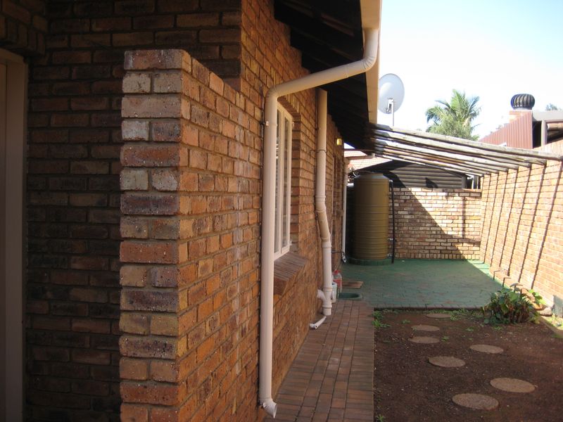 Rear exterior view featuring face brick walls, a rainwater storage tank, paved pathways, and a pergola structure along the side of the house.