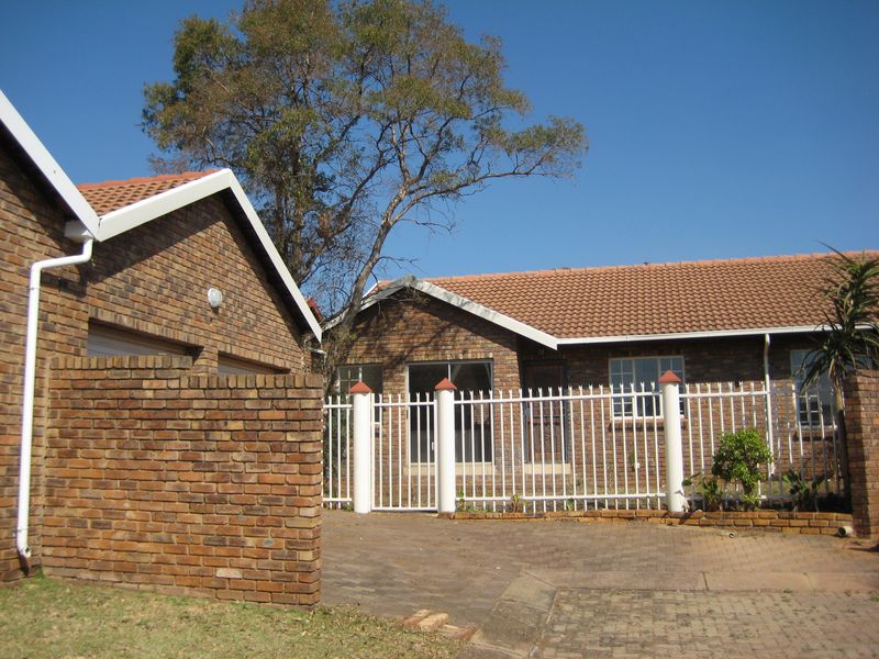 Front exterior view of a face brick house featuring a tiled roof, paved driveway, and secure perimeter fencing.