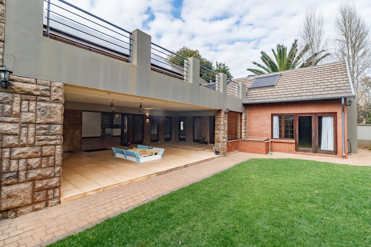 Spacious rear exterior featuring a large covered patio, upper balcony with metal railings, brick and stone facade, and a well-maintained garden lawn.