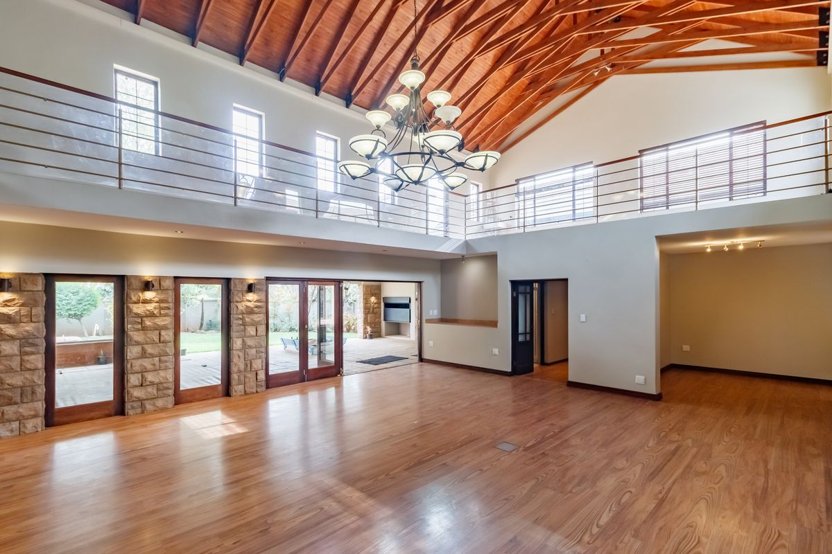 Spacious open-plan living area featuring high vaulted timber ceilings, a mezzanine level, stone accents, and large glass doors opening to the outdoor patio.