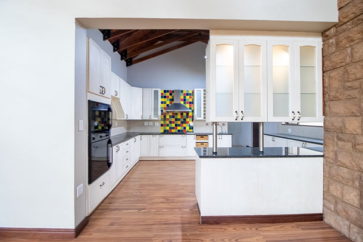 Spacious kitchen featuring white cabinetry, granite countertops, a vibrant tiled splashback, exposed timber trusses, and a unique stone-clad feature wall.