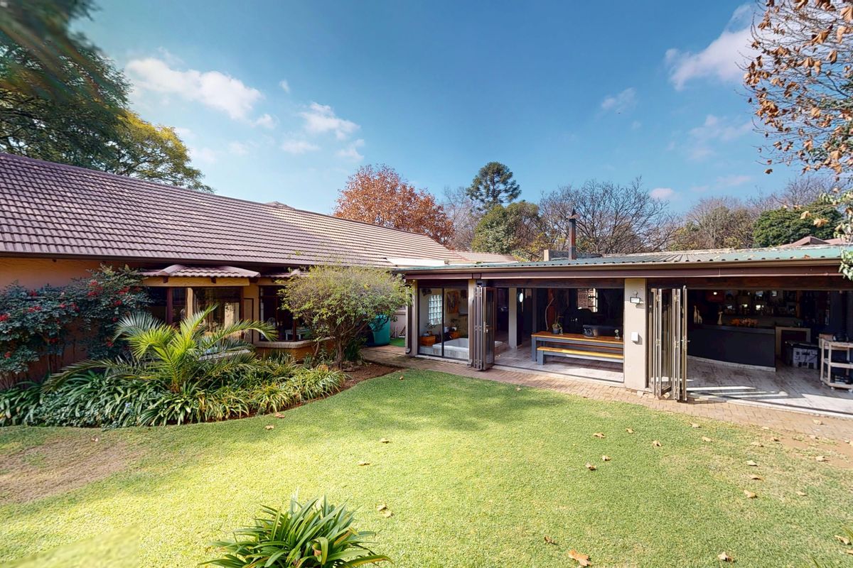 Rear view of the property featuring a well-maintained garden, brick paved patio, and a covered entertainment area with bi-fold doors opening to the lawn.