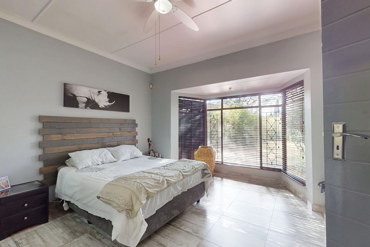 A well-lit bedroom featuring tiled flooring, a ceiling fan, and a large bay window with integrated security bars.