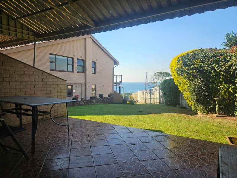 A covered patio area overlooking a private garden with ocean views in the distance.