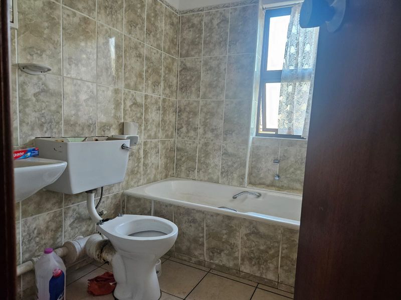 A dated bathroom featuring a built-in bathtub, wall-mounted basin, and toilet, finished with full-height ceramic wall tiles and tiled flooring.