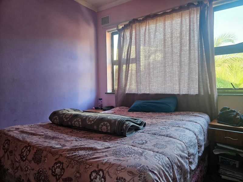 A bedroom featuring purple painted walls, an aluminium window frame, and a built-in air vent, requiring cosmetic updates to improve the overall aesthetic.
