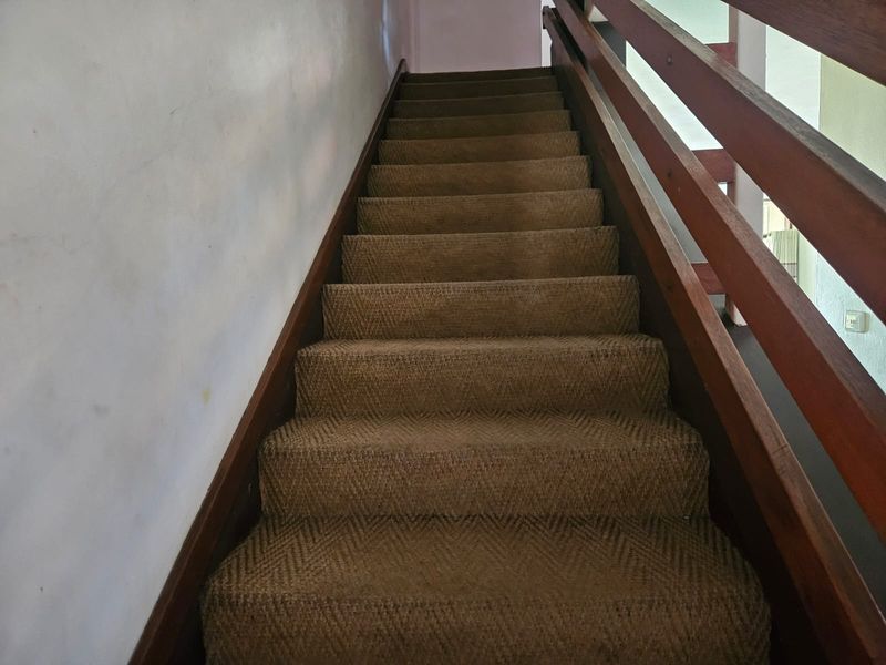 A staircase featuring a timber handrail and carpeted steps, providing access between levels in the townhouse.