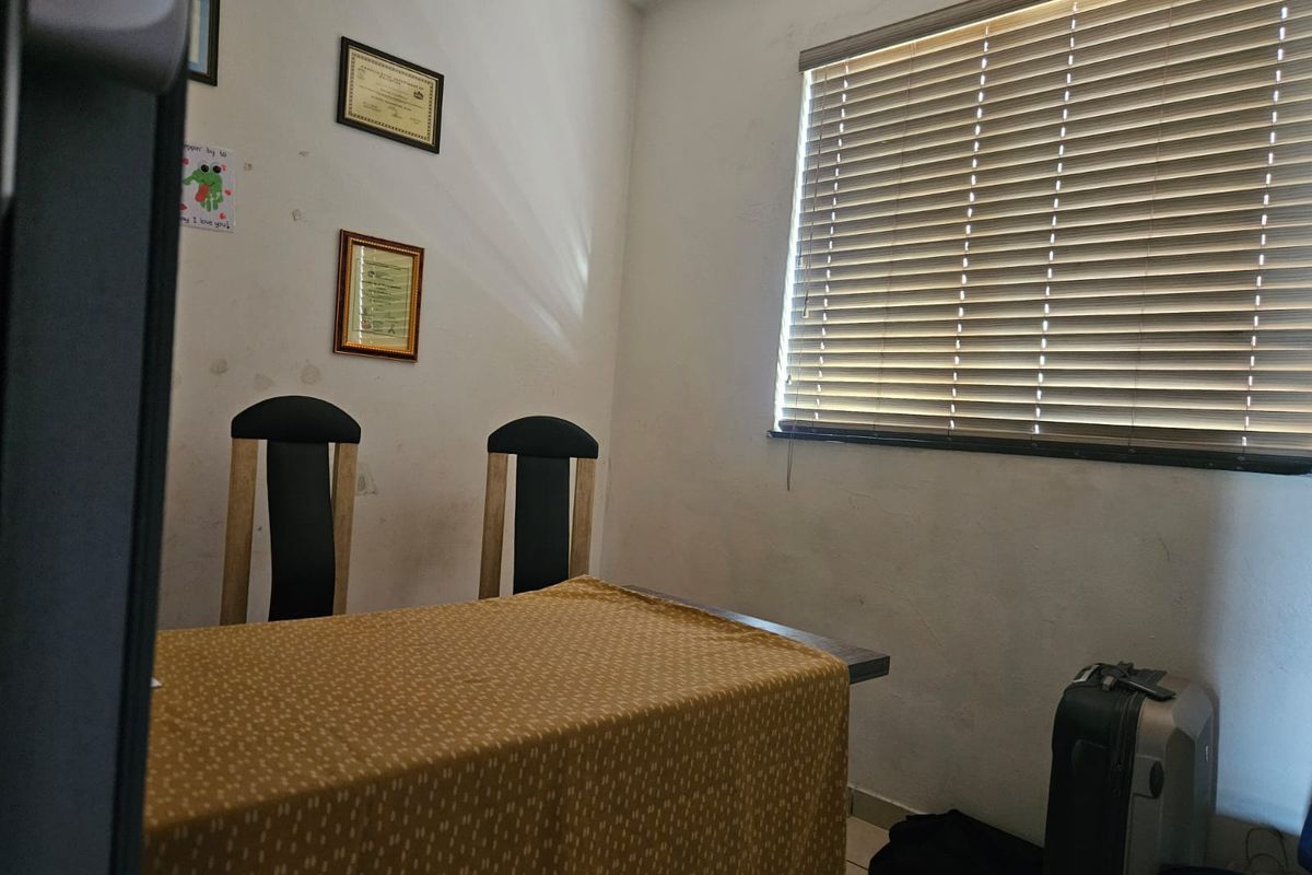 A bedroom featuring tiled flooring and venetian blinds, currently showing signs of wear on the walls requiring maintenance or cosmetic updates.