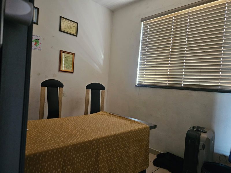 A bedroom featuring tiled flooring and venetian blinds, currently showing signs of wear on the walls requiring maintenance or cosmetic updates.