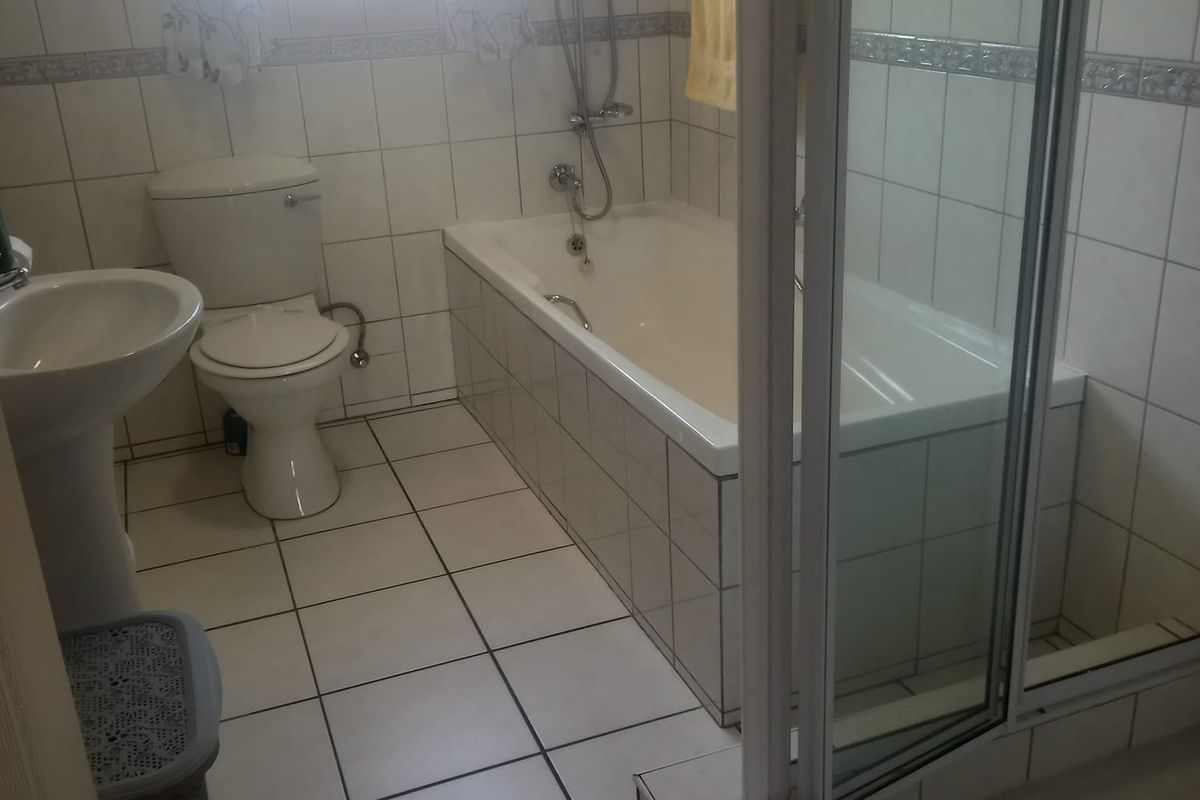 A functional bathroom featuring a pedestal basin, toilet, built-in bathtub, and a separate glass-enclosed shower with full-height wall tiling.