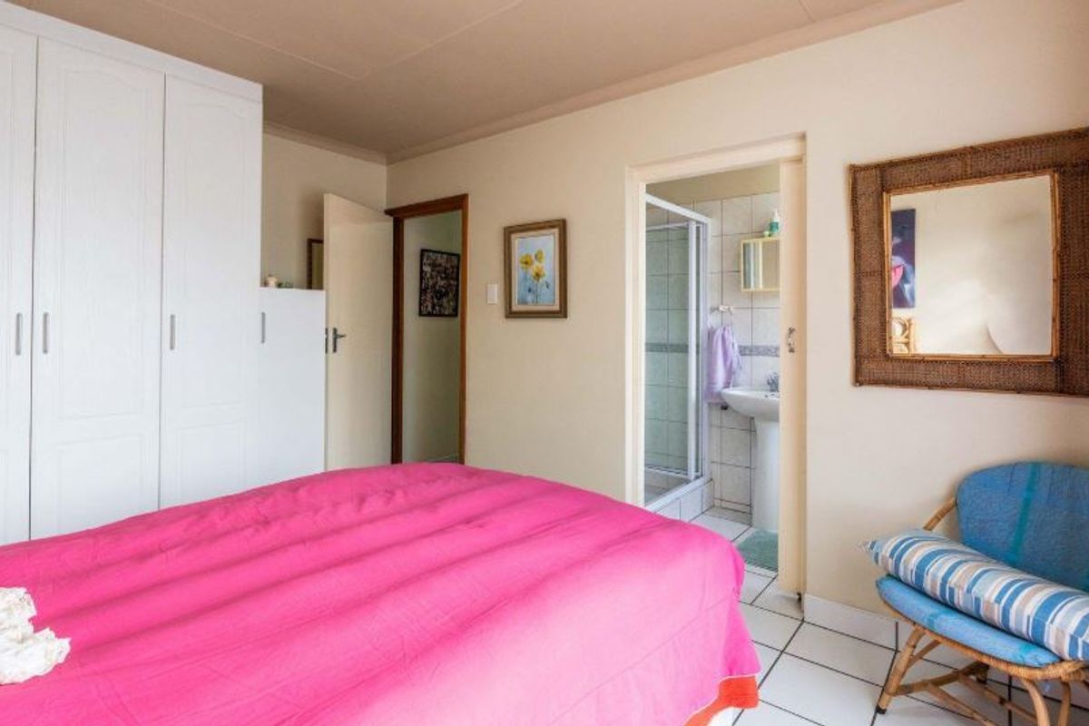 A bedroom featuring built-in cupboards and an en-suite bathroom with a shower and pedestal basin, finished with tiled flooring.