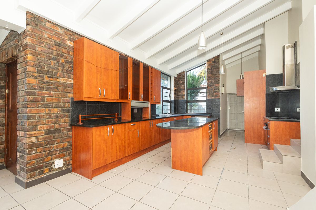 Spacious kitchen featuring wooden cabinetry, granite countertops, a central island, and exposed brick walls under a high vaulted ceiling with exposed beams.
