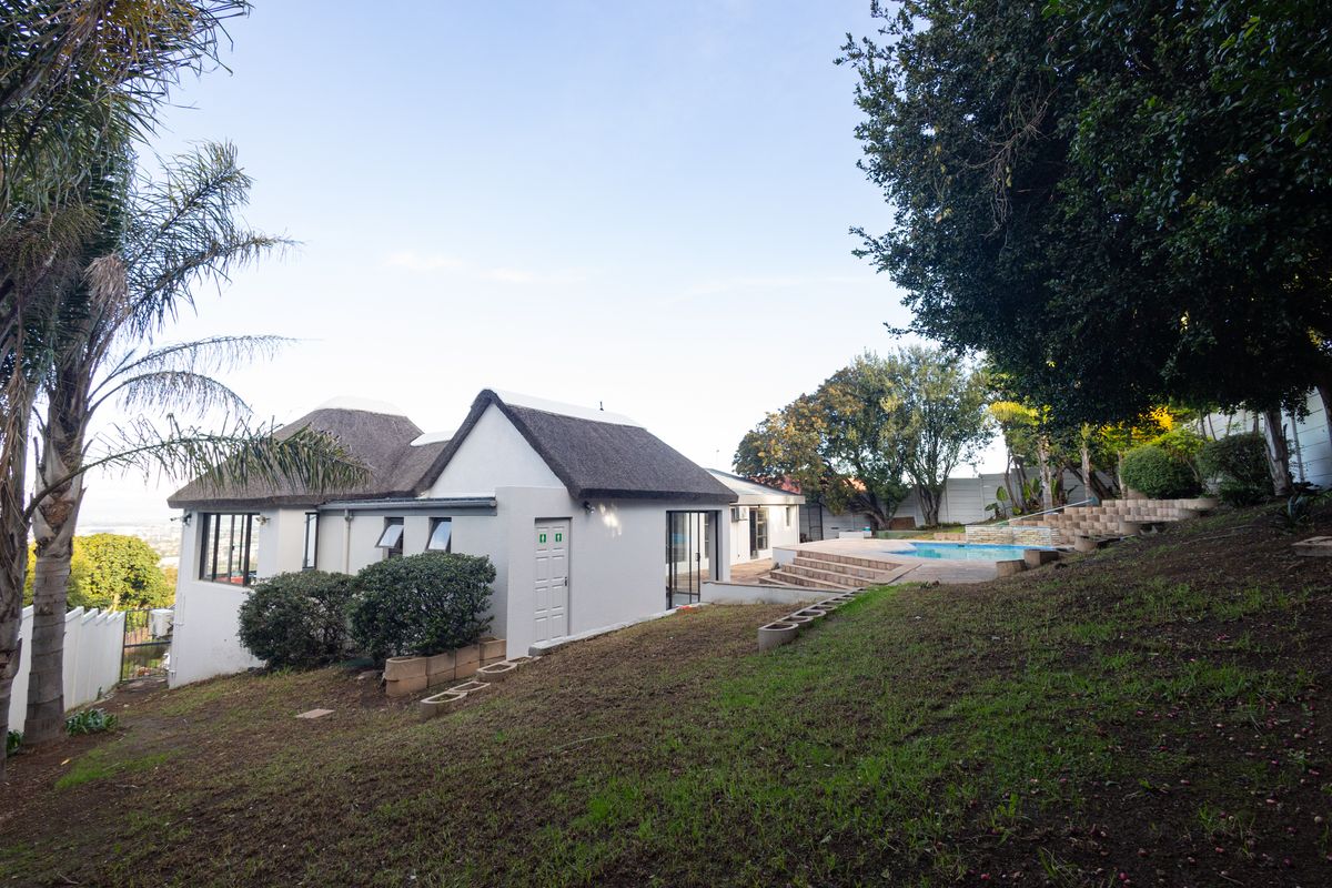 Rear view of the property featuring a thatched roof house, a swimming pool, and a tiered garden area.