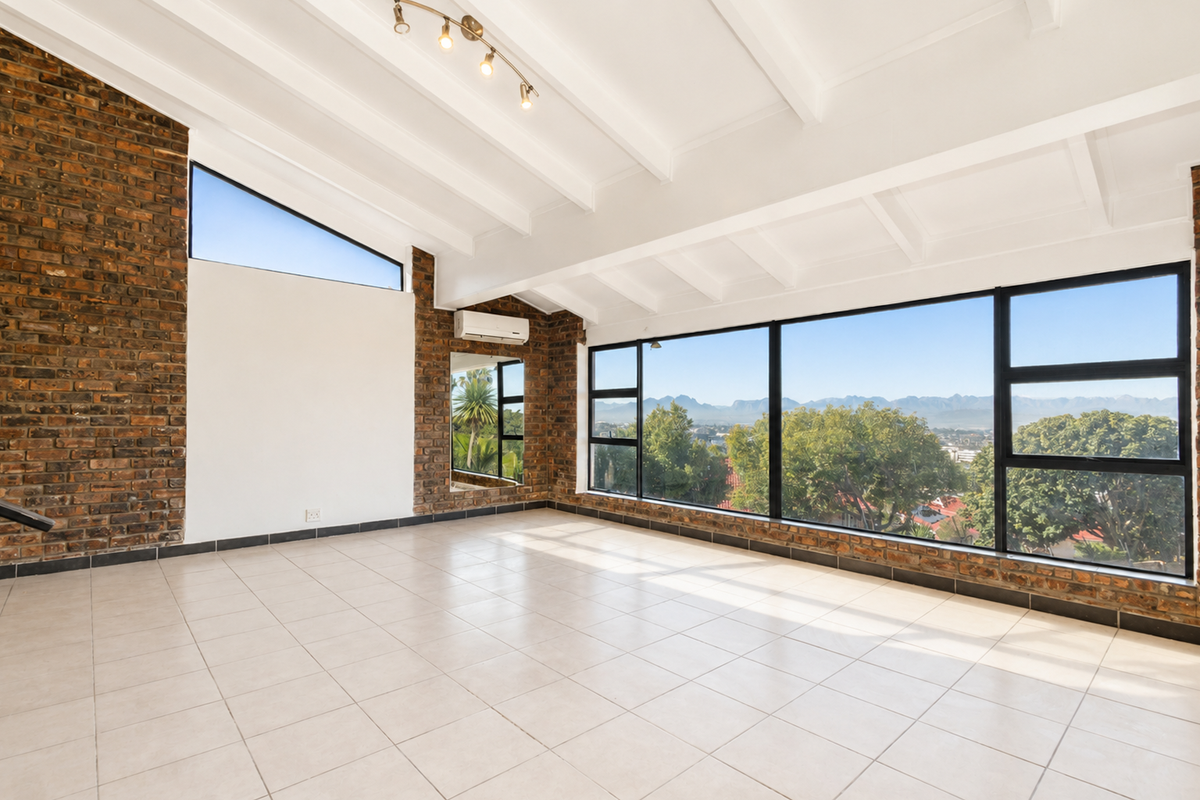 Spacious living area featuring exposed brick walls, vaulted beamed ceilings, large windows with scenic mountain views, and a wall-mounted air conditioning unit.
