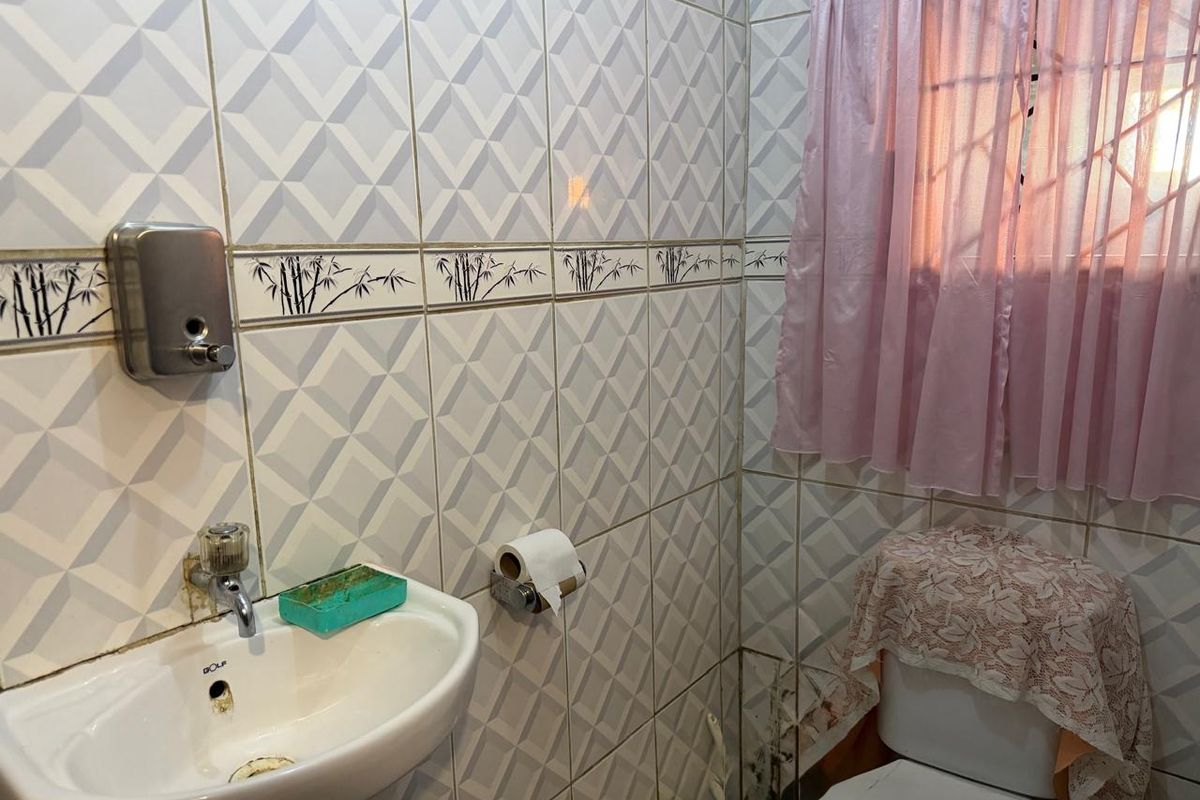 A compact bathroom featuring wall-mounted basin, toilet, and decorative ceramic wall tiling with security bars on the window.