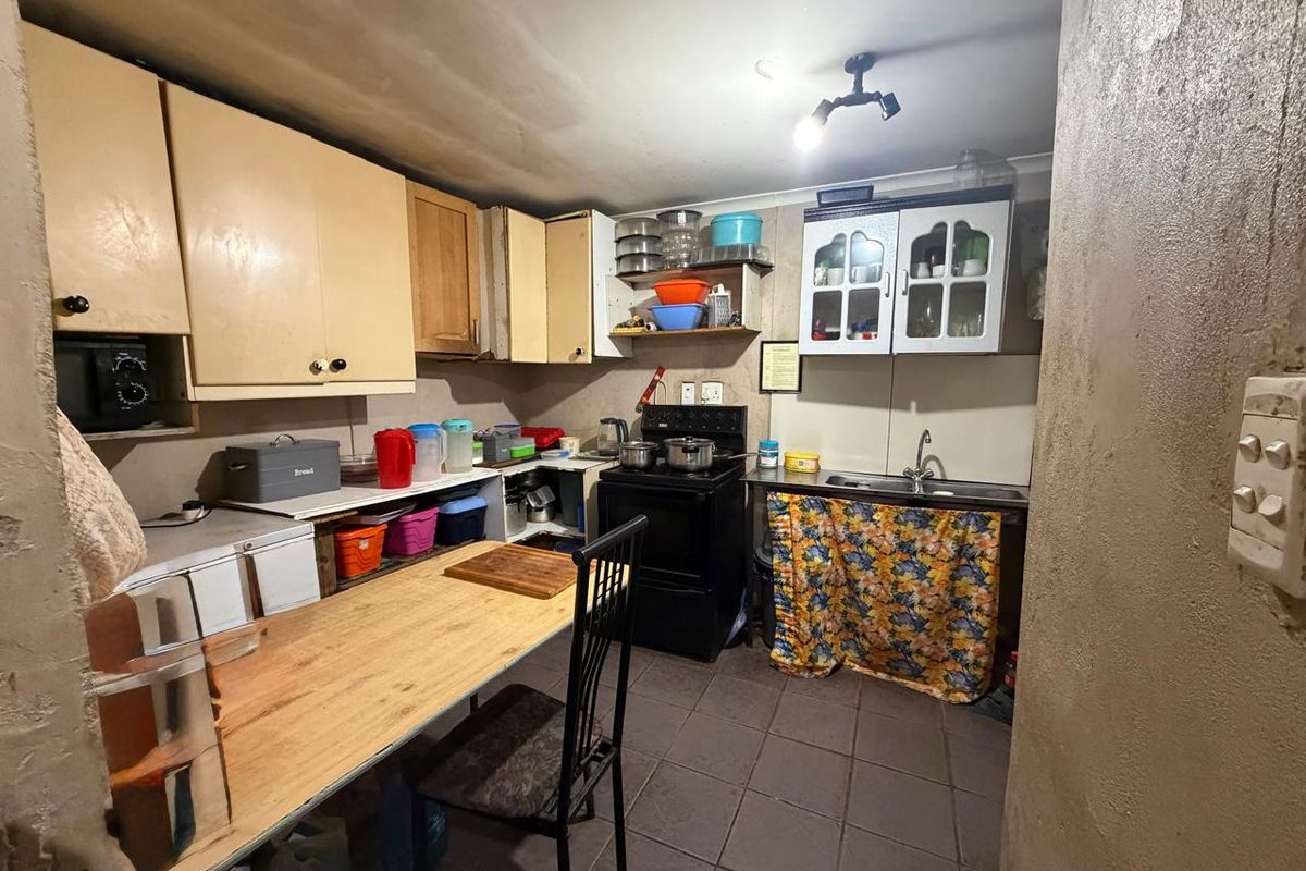 A compact kitchen featuring dated cabinetry, tiled flooring, and a functional layout with a stainless steel sink and freestanding stove.