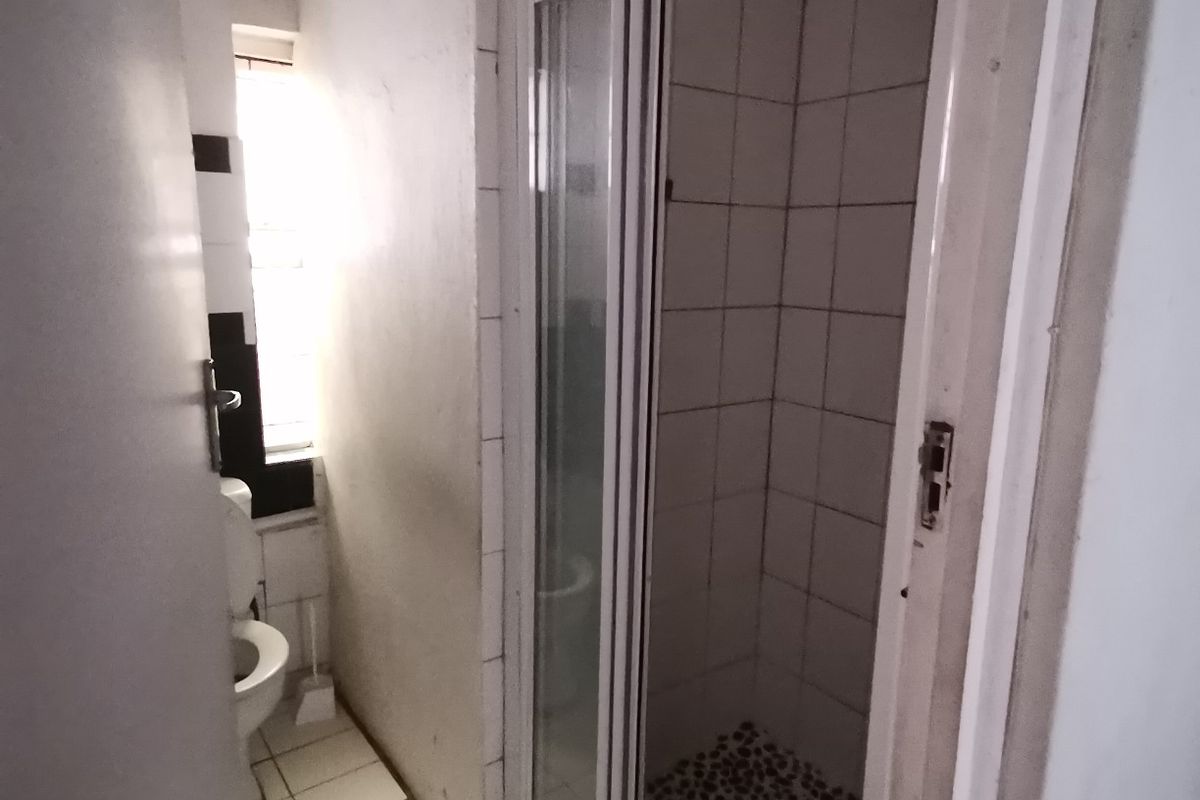 A compact bathroom featuring a shower enclosure with pebble-style flooring, white wall tiles, and a standard toilet.