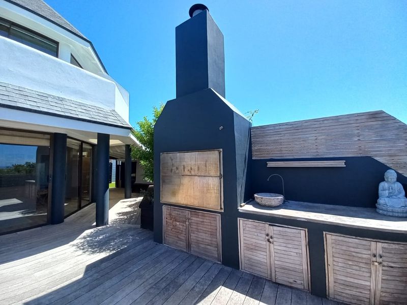 Outdoor entertainment area featuring a built-in braai, stone basin, and timber cabinetry set on a wooden deck.