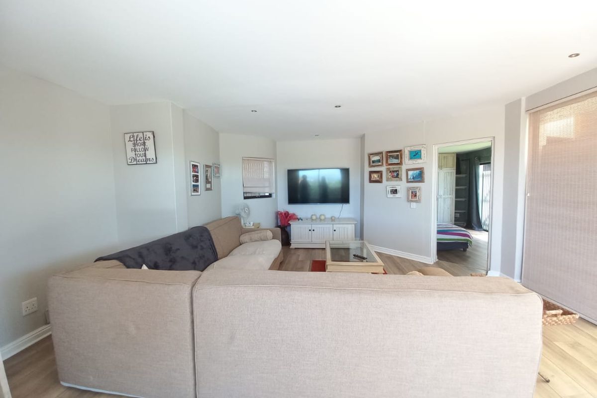 A comfortable living room featuring light-toned laminate flooring, recessed ceiling lighting, and a neutral color palette, providing a bright and inviting atmosphere.
