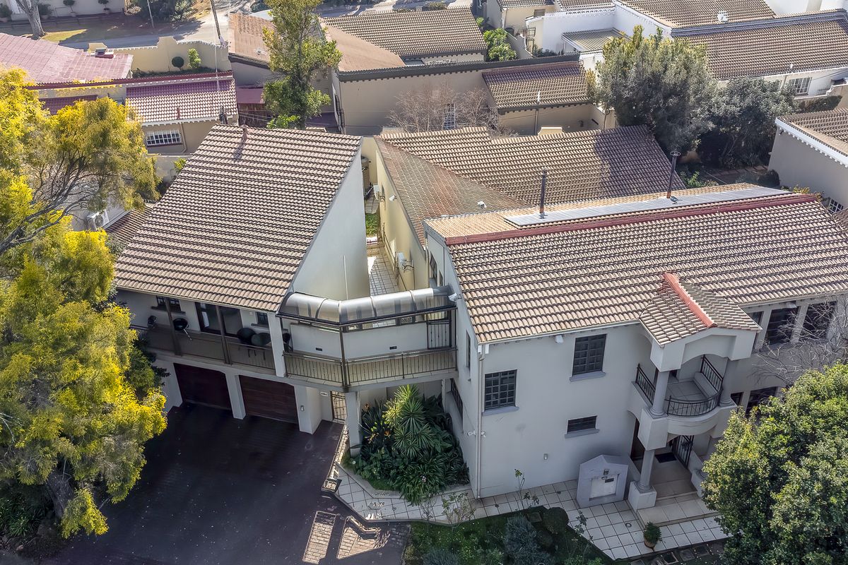 Aerial view of a multi-level residential property featuring a tiled roof, double garage, and balcony, situated within a suburban estate setting.
