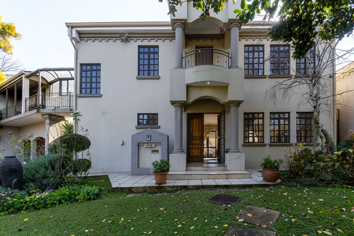Rear view of a multi-story residence featuring a tiled patio, balcony with wrought iron railings, and established garden landscaping.