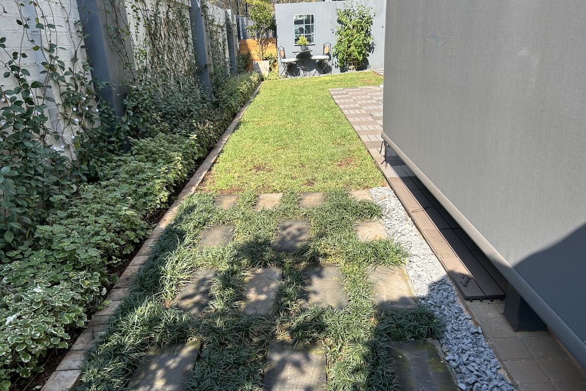 A well-maintained rear garden featuring a paved walkway, lush lawn, and established boundary wall landscaping.
