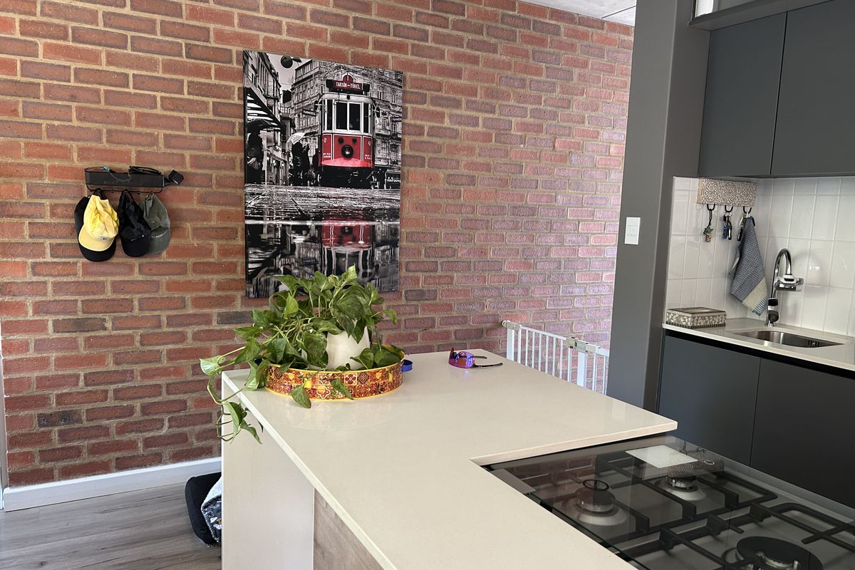 Modern kitchen featuring a central island with a built-in gas cooktop, sleek dark cabinetry, and a distinctive exposed brick feature wall.