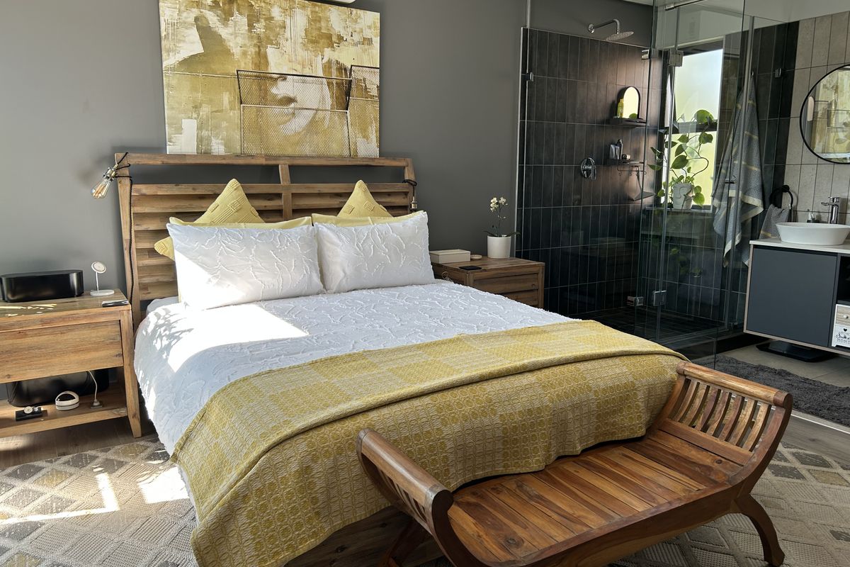 Modern bedroom featuring an open-plan en-suite bathroom with a glass-enclosed shower, floating vanity, and wall-mounted air conditioning unit.