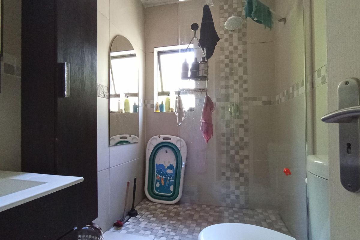 A functional bathroom featuring a tiled shower enclosure with a glass screen, a vanity cabinet, and neutral wall tiling.