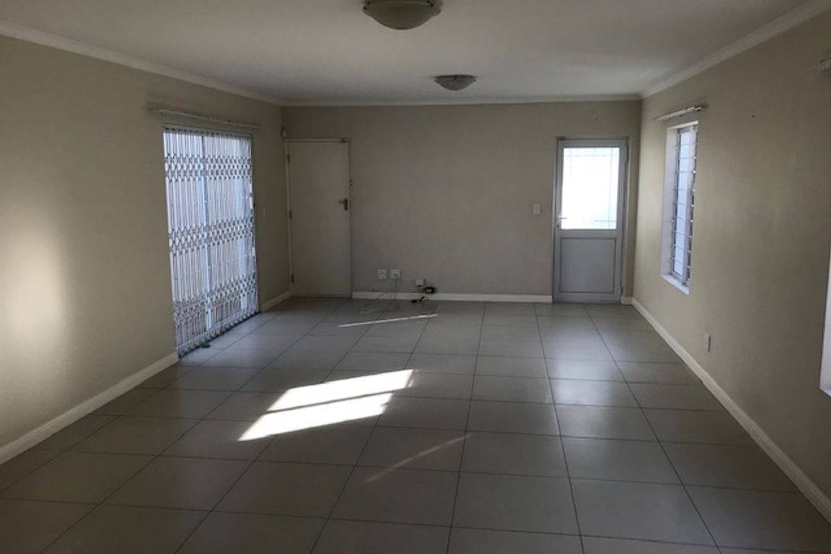 A spacious, empty living area featuring neutral tiled flooring, ceiling-mounted light fixtures, and secure metal security gates on the sliding glass doors.