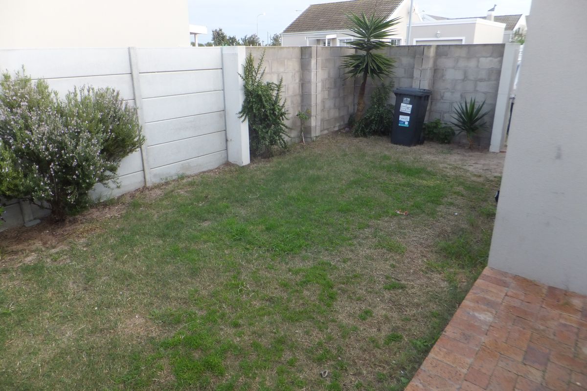 A compact rear garden area featuring a small lawn, paved patio section, and concrete block boundary walls.
