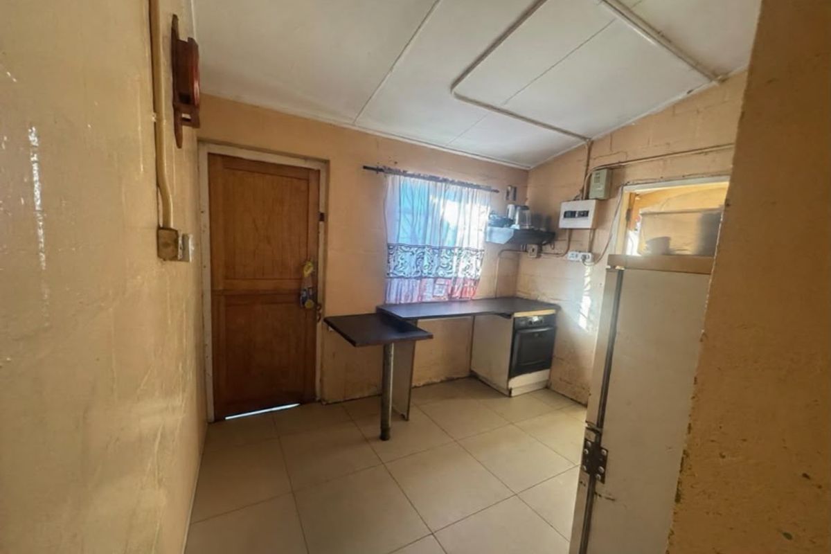 A compact kitchen area featuring tiled flooring, a built-in oven, and a timber door, requiring cosmetic updates to improve its overall condition.