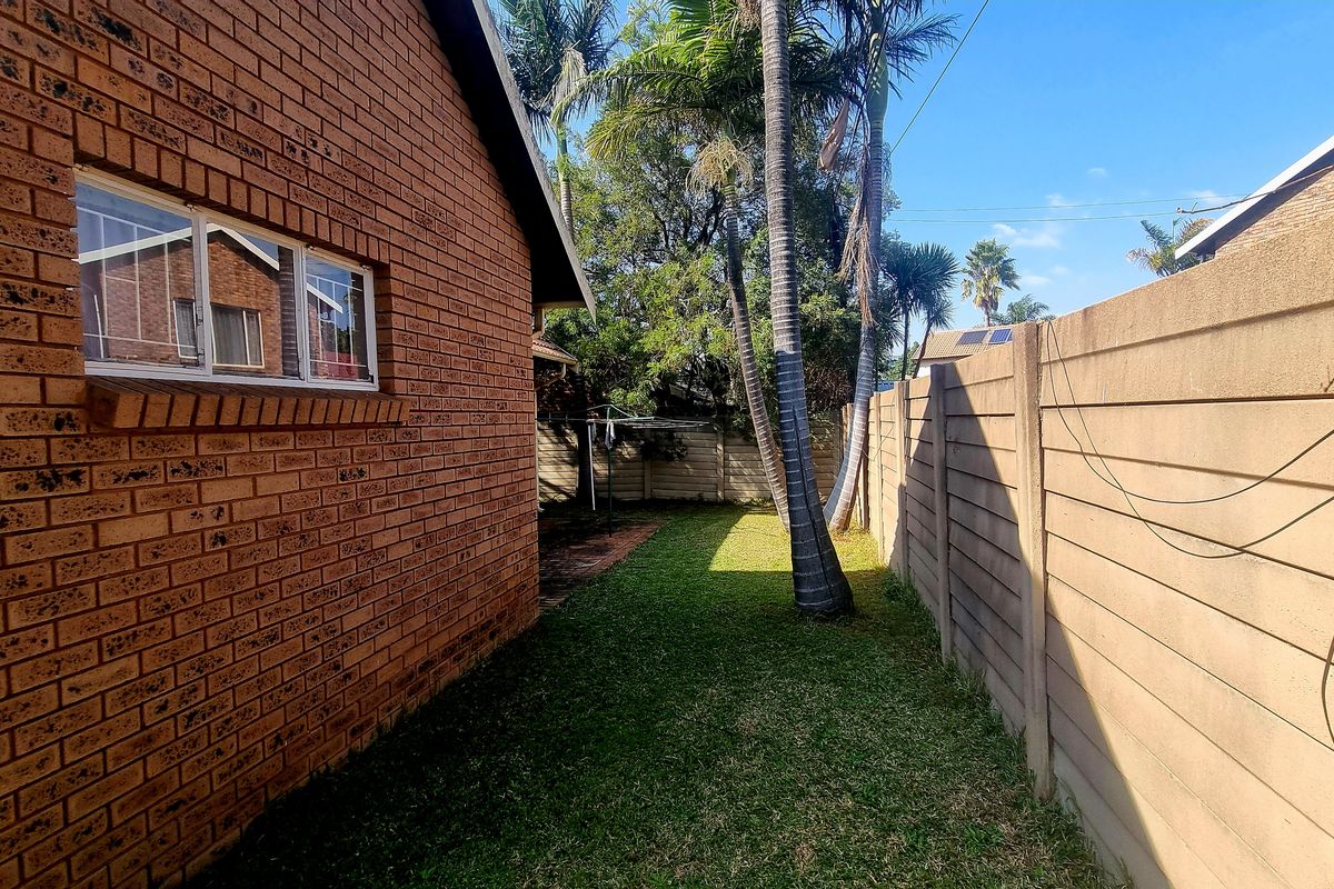 A side garden area featuring a brick exterior wall, a lawn, and a precast concrete boundary wall.