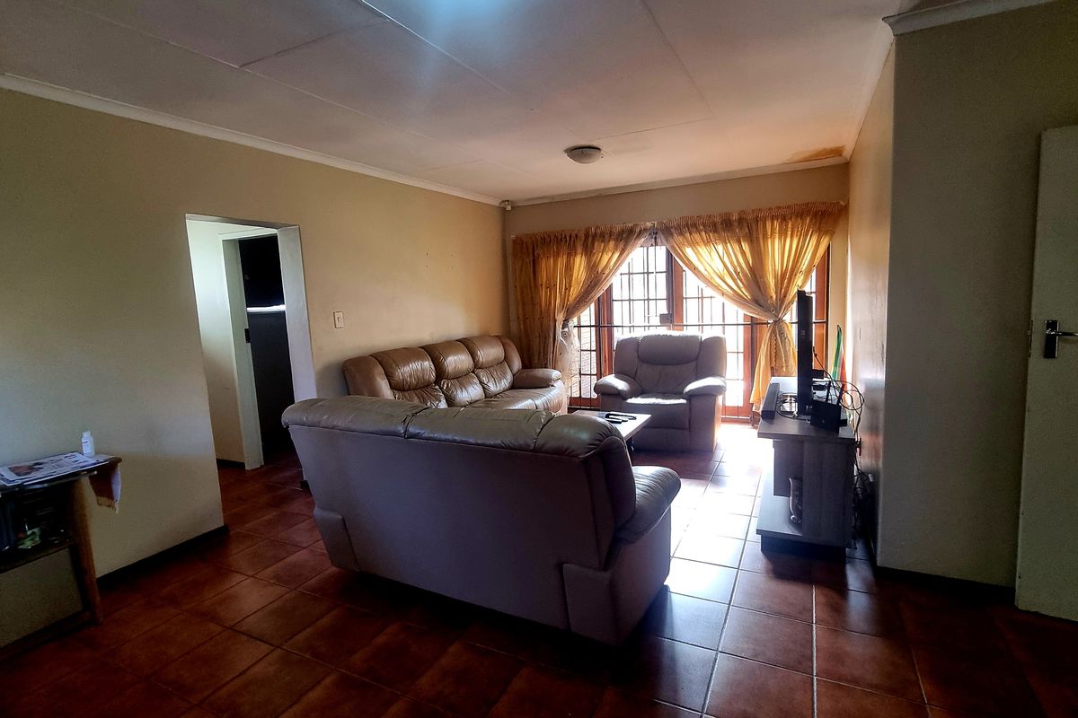 A living room featuring tiled flooring, a ceiling with visible water staining, and sliding door access to the exterior.