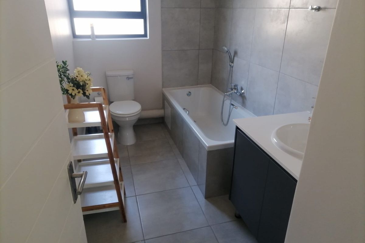 Modern bathroom featuring large format grey floor and wall tiles, a built-in bathtub with shower mixer, and a contemporary vanity unit.