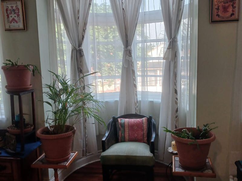 A cozy living room area featuring a large bay window with natural light, hardwood flooring, and classic architectural details like picture rails.