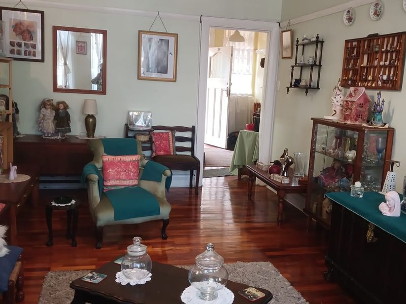 A living room featuring polished hardwood flooring, a classic picture rail, and a central pendant light fixture, leading through to an adjacent room.