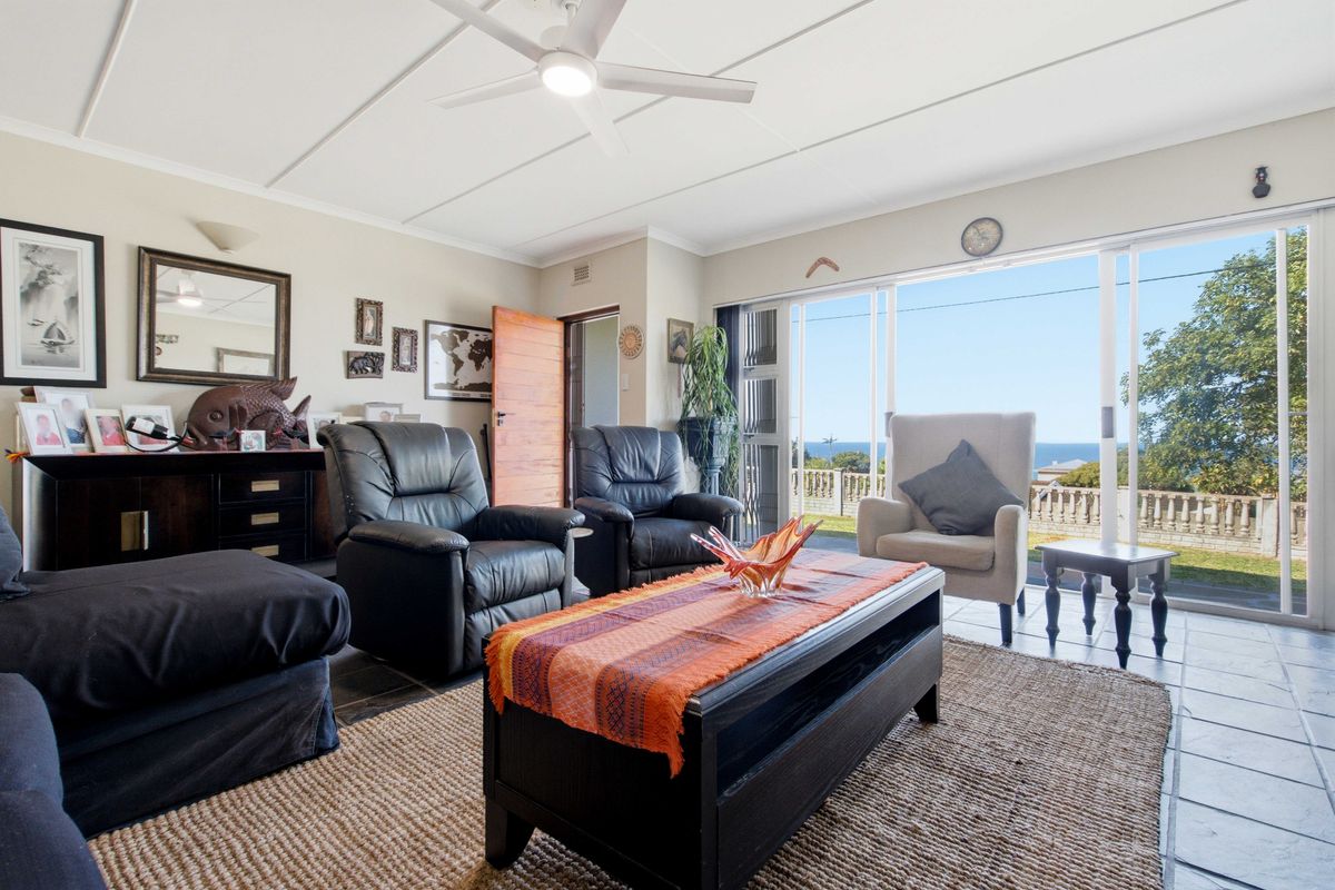 A bright living room featuring tiled flooring, a ceiling fan, and large sliding glass doors that open to an outdoor area with ocean views.