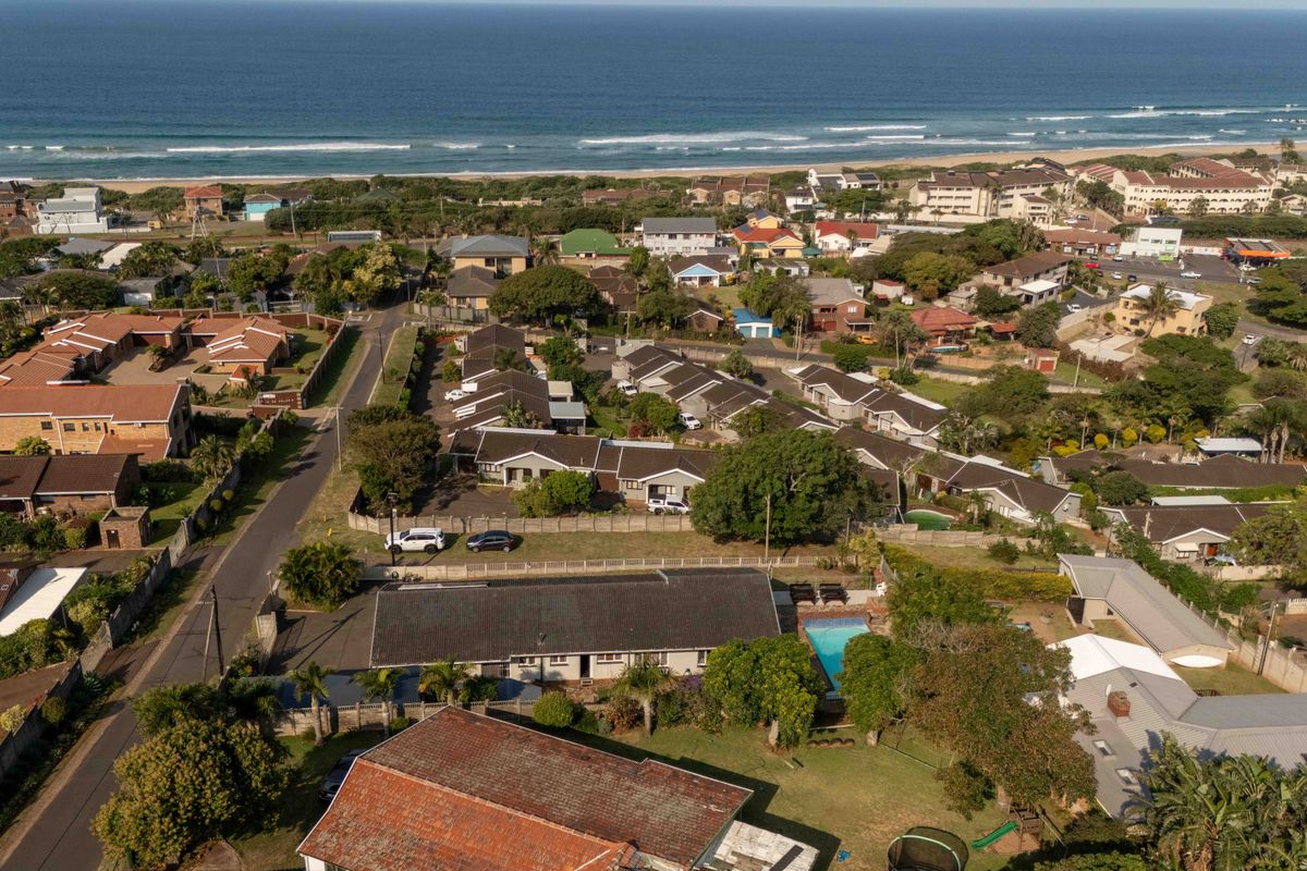 Aerial view of a residential property featuring a swimming pool, tiled roof, and established garden, situated in a coastal neighborhood near the beach.