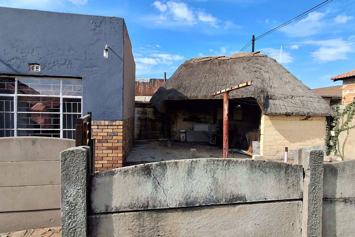 Rear exterior view of the property featuring a thatched roof structure and a precast concrete boundary wall showing signs of wear and maintenance needs.