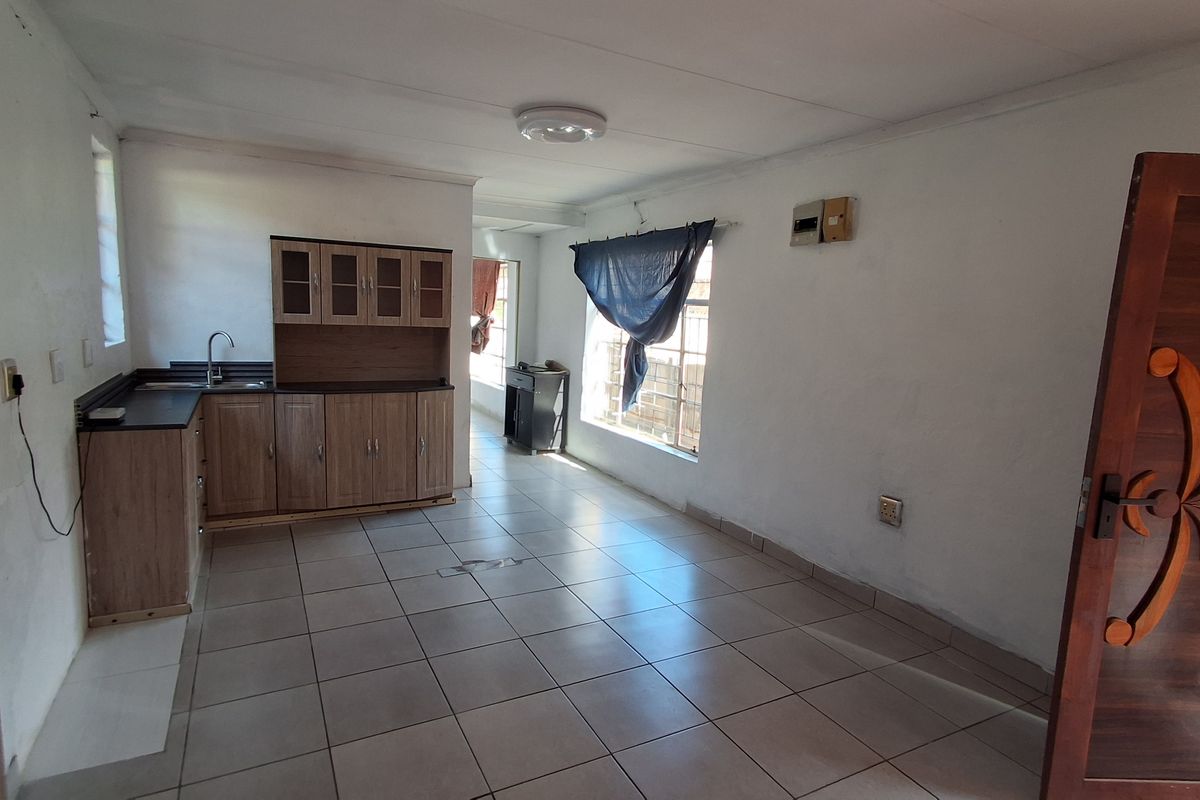 Open-plan living and kitchen area featuring tiled flooring, built-in cabinetry, and a functional sink, offering a blank canvas for renovation and interior design.