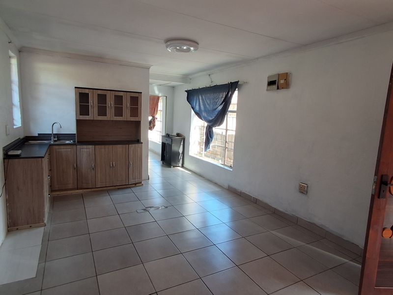 Open-plan living and kitchen area featuring tiled flooring, built-in cabinetry, and a functional sink, offering a blank canvas for renovation and interior design.