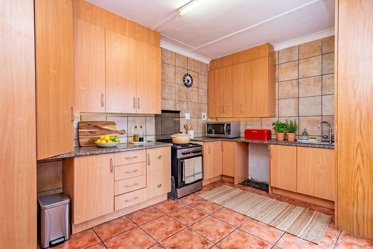A functional kitchen featuring light wood laminate cabinetry, granite countertops, tiled backsplash, and tiled flooring, offering a classic layout with integrated storage.