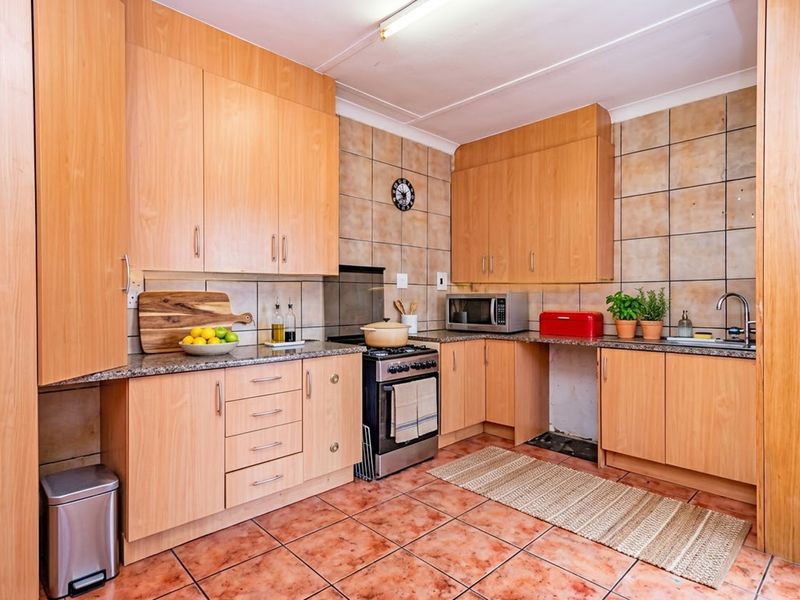 A functional kitchen featuring light wood laminate cabinetry, granite countertops, tiled backsplash, and tiled flooring, offering a classic layout with integrated storage.
